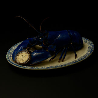 Montre gousset en argent déposée dans la pince d'un homard bleu.